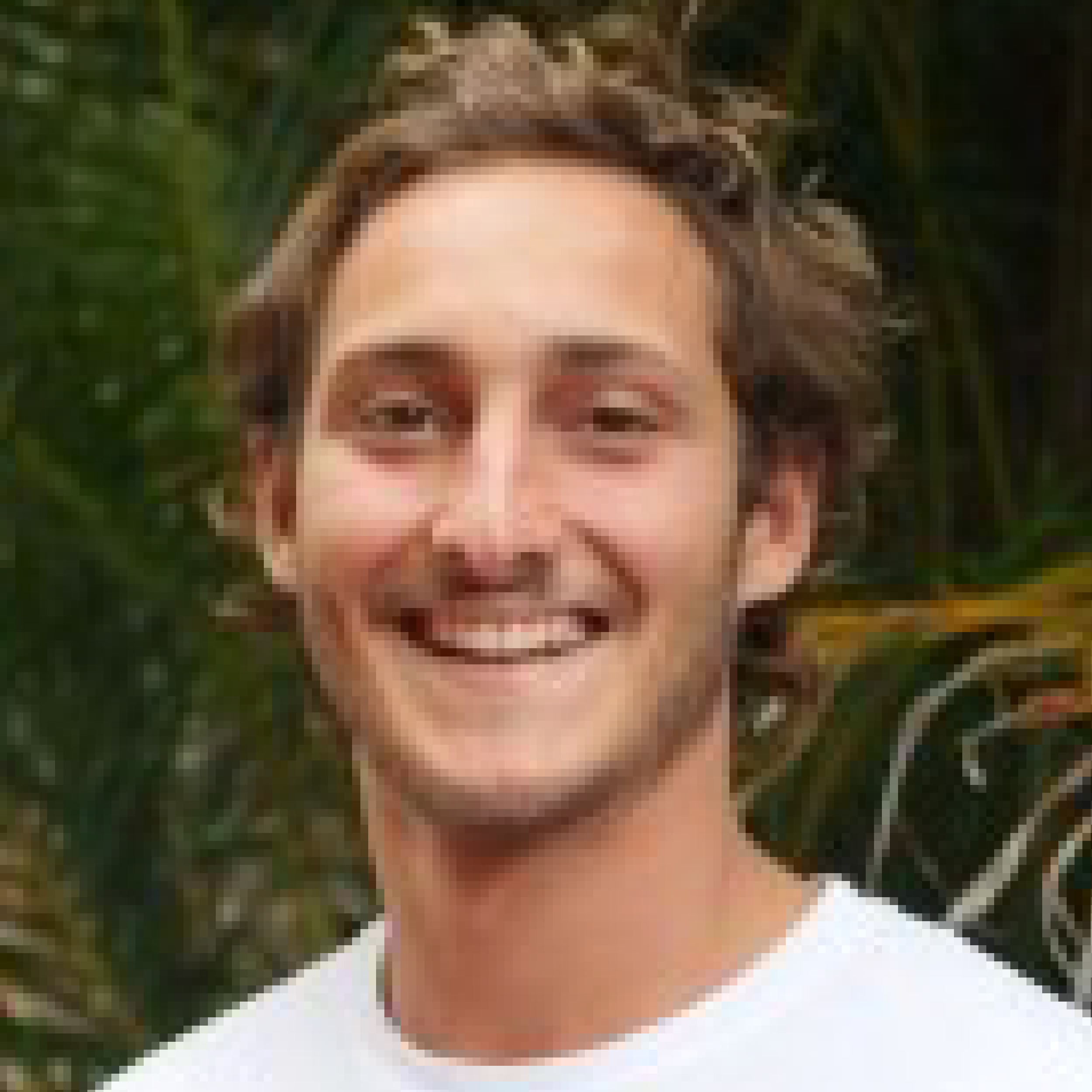 Smiling man outdoors with trees in background.