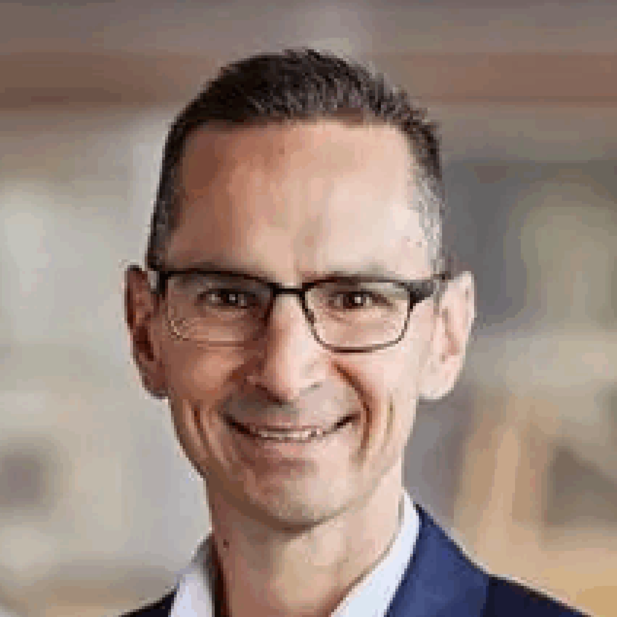 Man wearing glasses, smiling in professional attire.