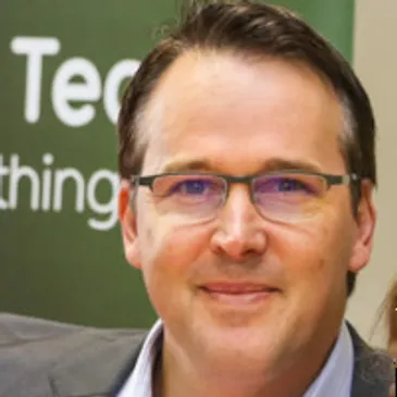 Man smiling, wearing glasses and suit jacket.