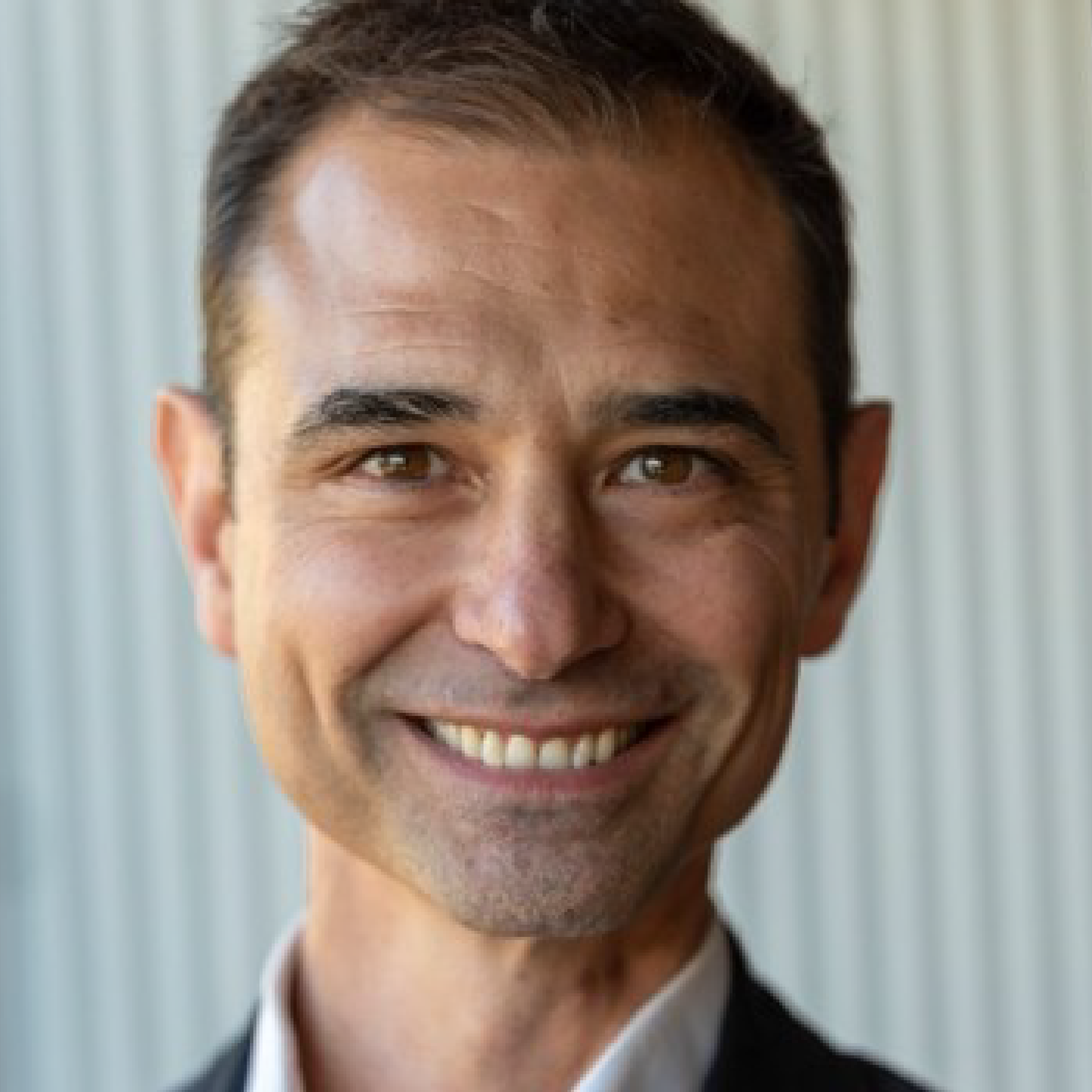 Smiling man in a suit, neutral background.