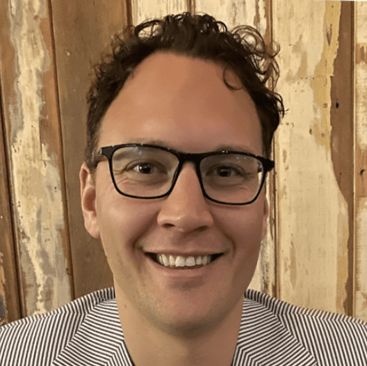 Man wearing glasses, smiling in striped blazer.